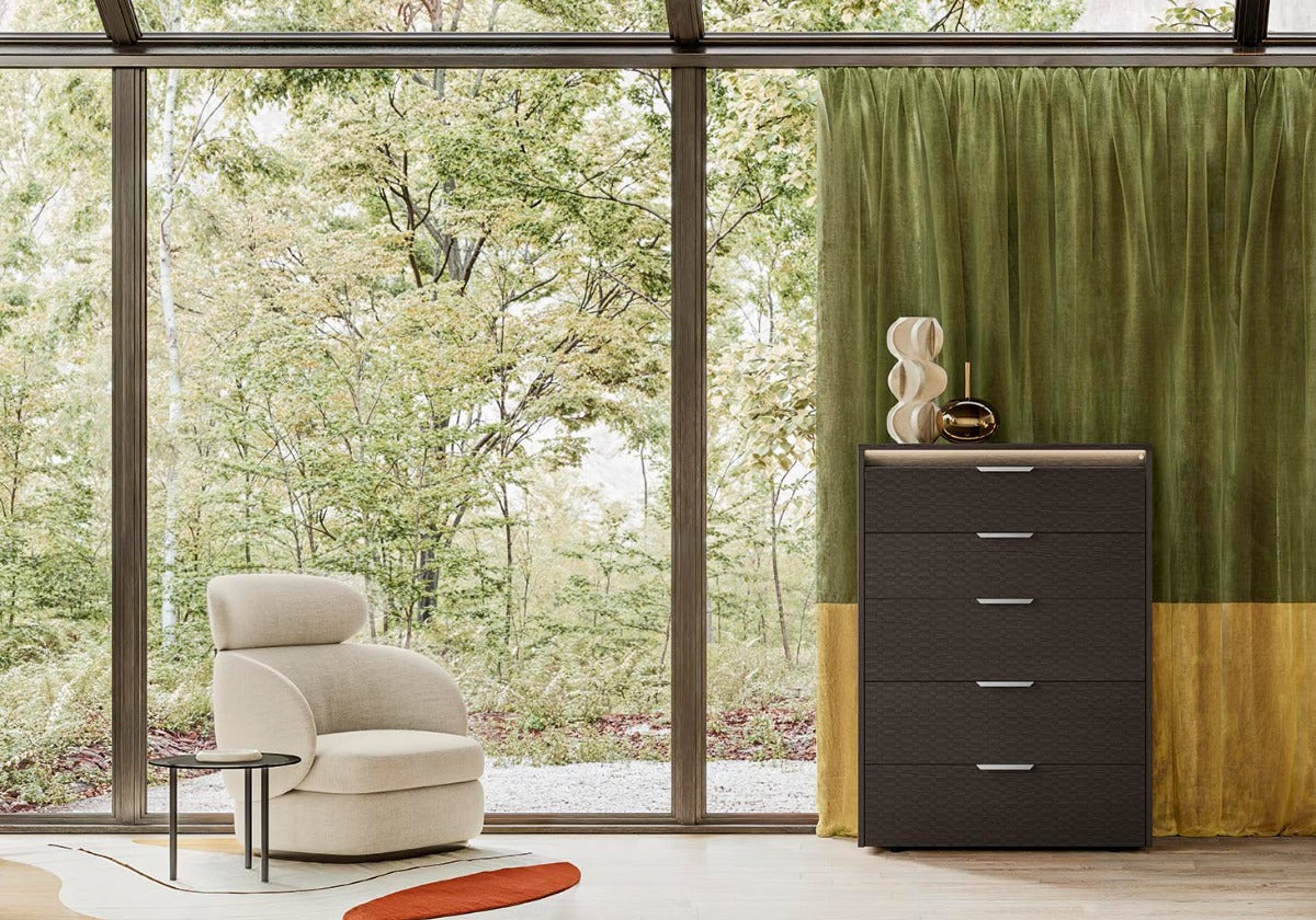 Modern interior with a beige armchair, dark brown and yellow chest of drawers, and green curtain.