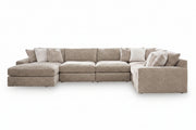 A light beige upholstered sectional sofa with a left-facing chaise lounge and multiple matching accent pillows, shown against a plain white background.