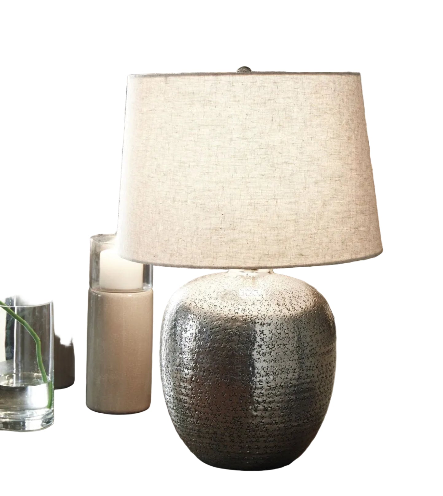 Decorative lamp with textured base on a table with candles and books in front of abstract wall art.