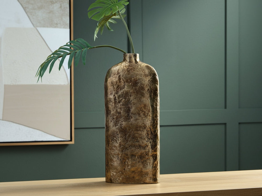 Decorative vase with a plant on a wooden surface against a green wall.