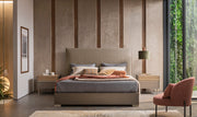 A stylish modern bedroom features an upholstered bed with a woven tan headboard and grey linens flanked by minimalist nightstands and a terracotta armchair.
