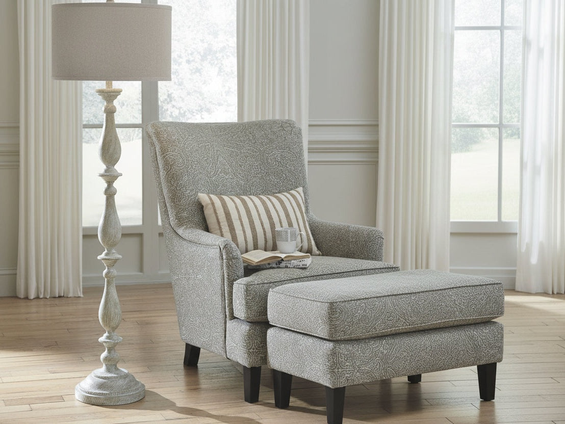Gray armchair with striped pillow next to a tall white floor lamp in a room with large windows.
