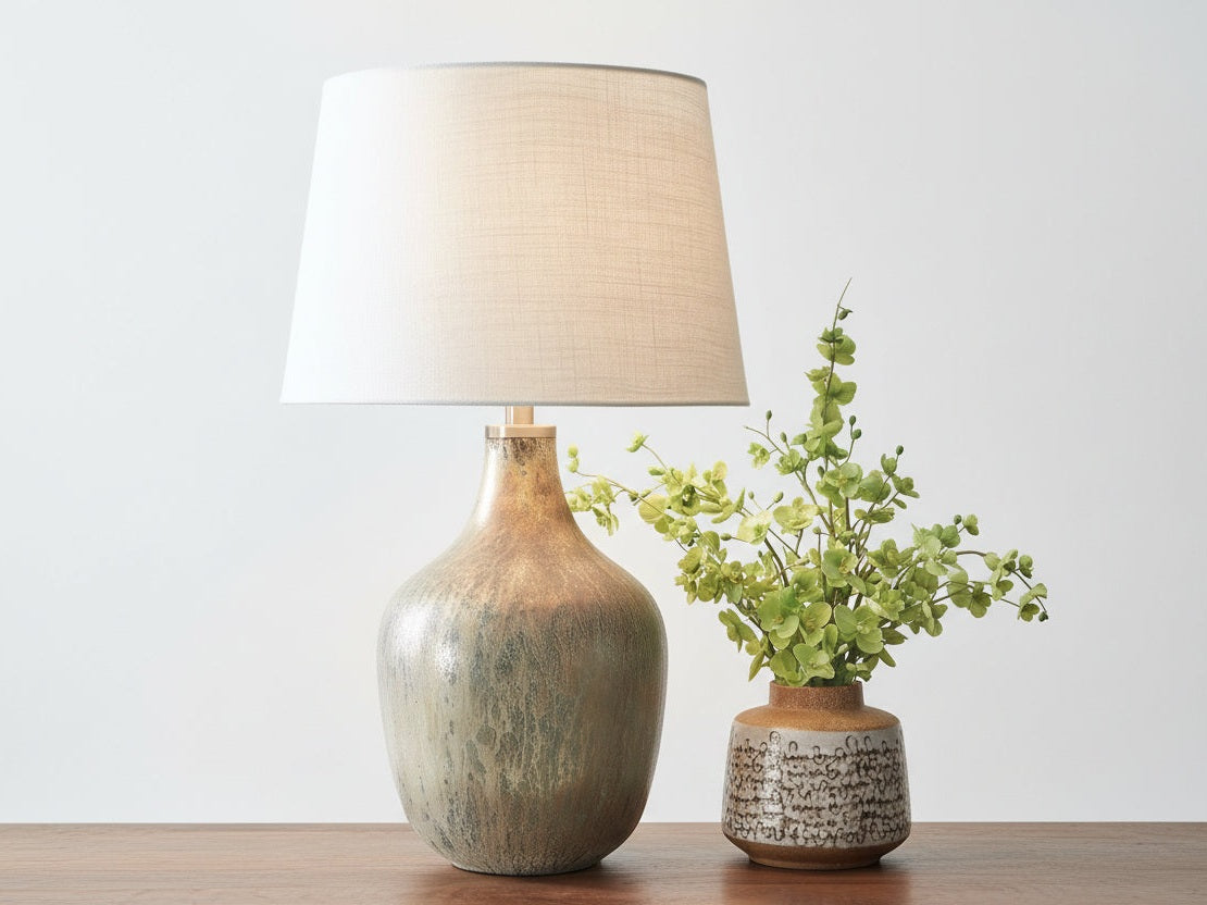 Mari decorative lamp and small plant on a wooden surface with a plain background.