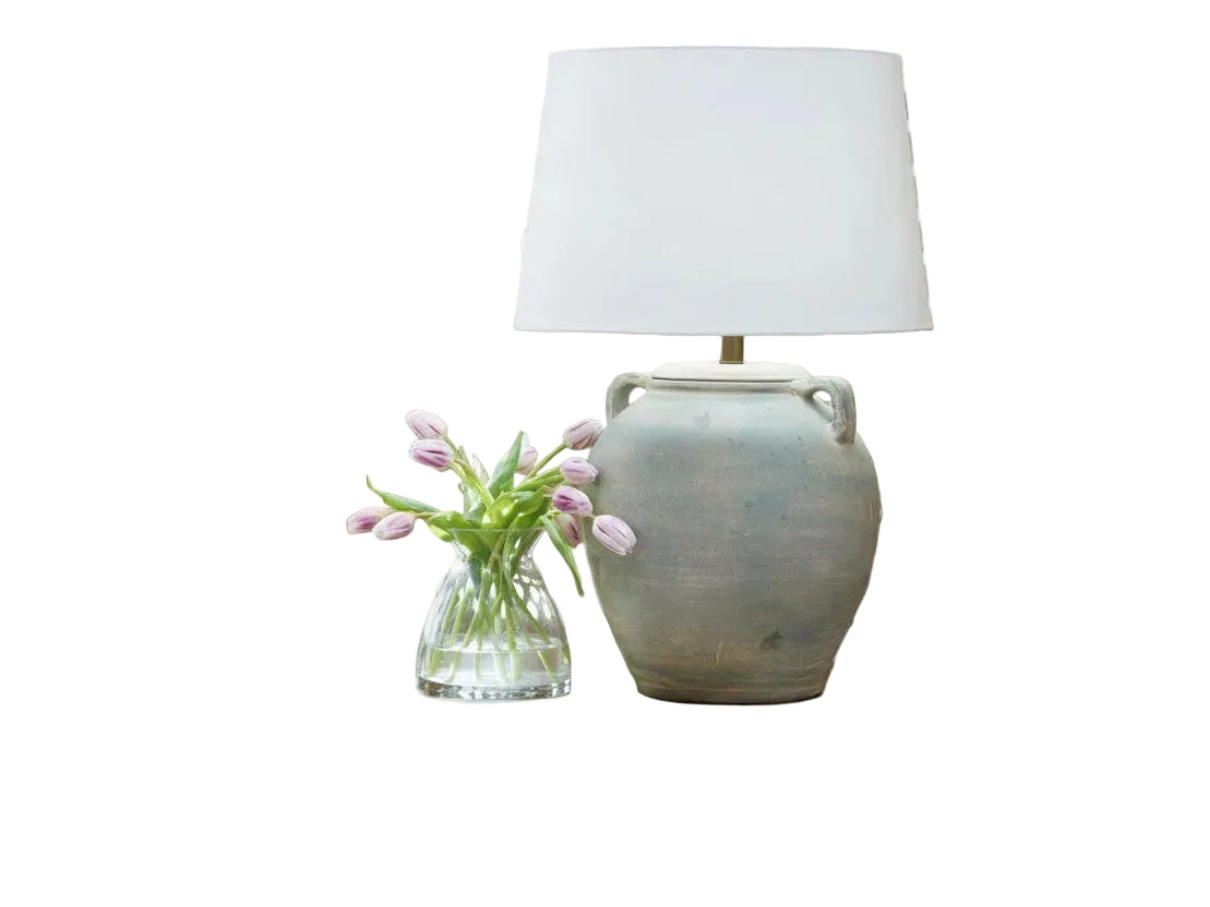 A Shawburg decorative lamp on a wooden table with a vase of flowers and books against a patterned wall.