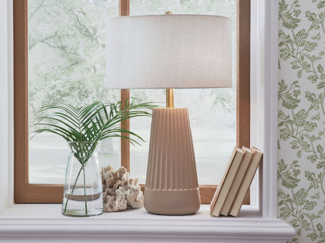 The Dellner beige table lamp on a windowsill with a plant and books in the background.