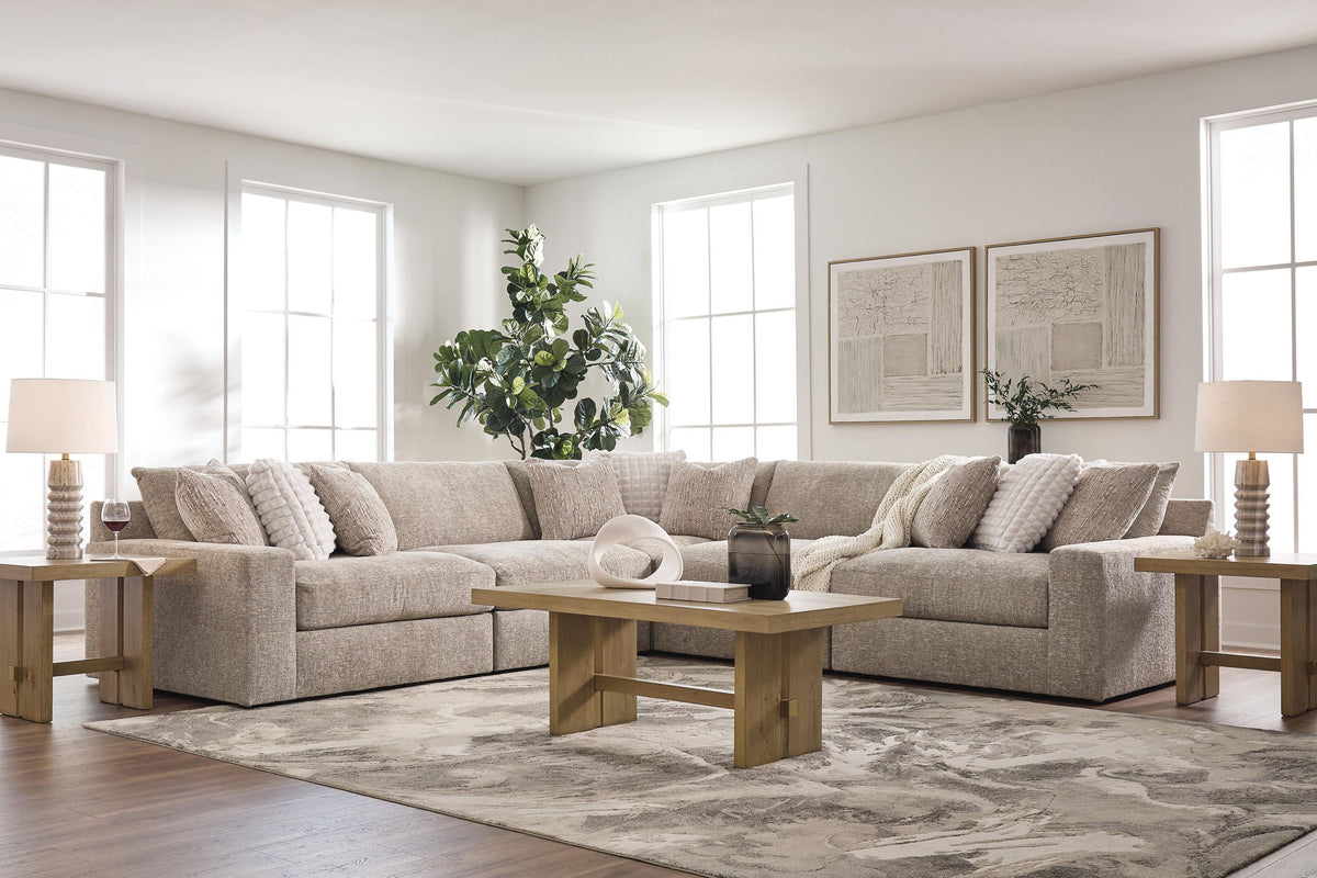 A light beige upholstered sectional sofa in a bright, modern living room with a wooden coffee table, side tables, lamps, and a patterned area rug.