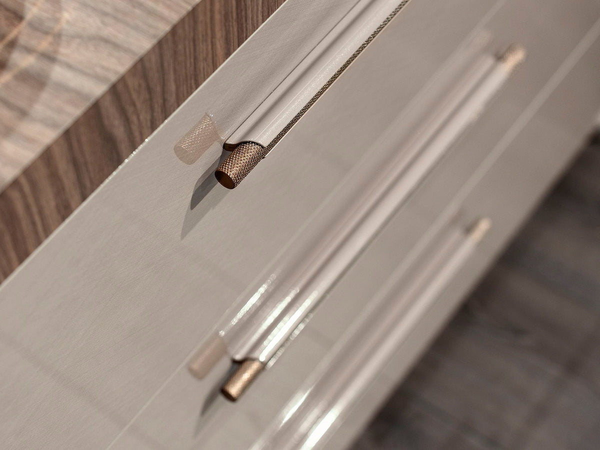Close-up of modern cabinet handles with a brushed silver metal body and a textured bronze end cap, mounted on a light gray wood-grain cabinet door.