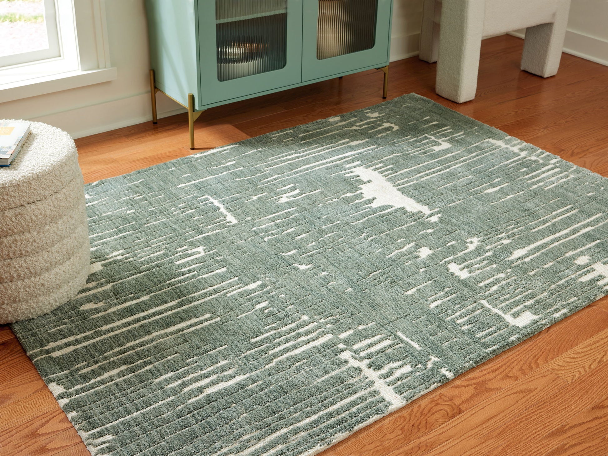 Green patterned rug on a wooden floor with a cabinet in the background