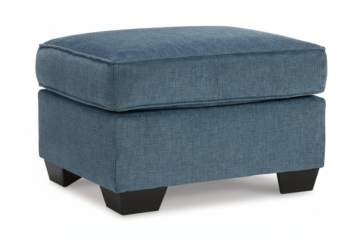 A blue upholstered ottoman with a textured fabric cover and dark wooden legs, shown on a clean white background.