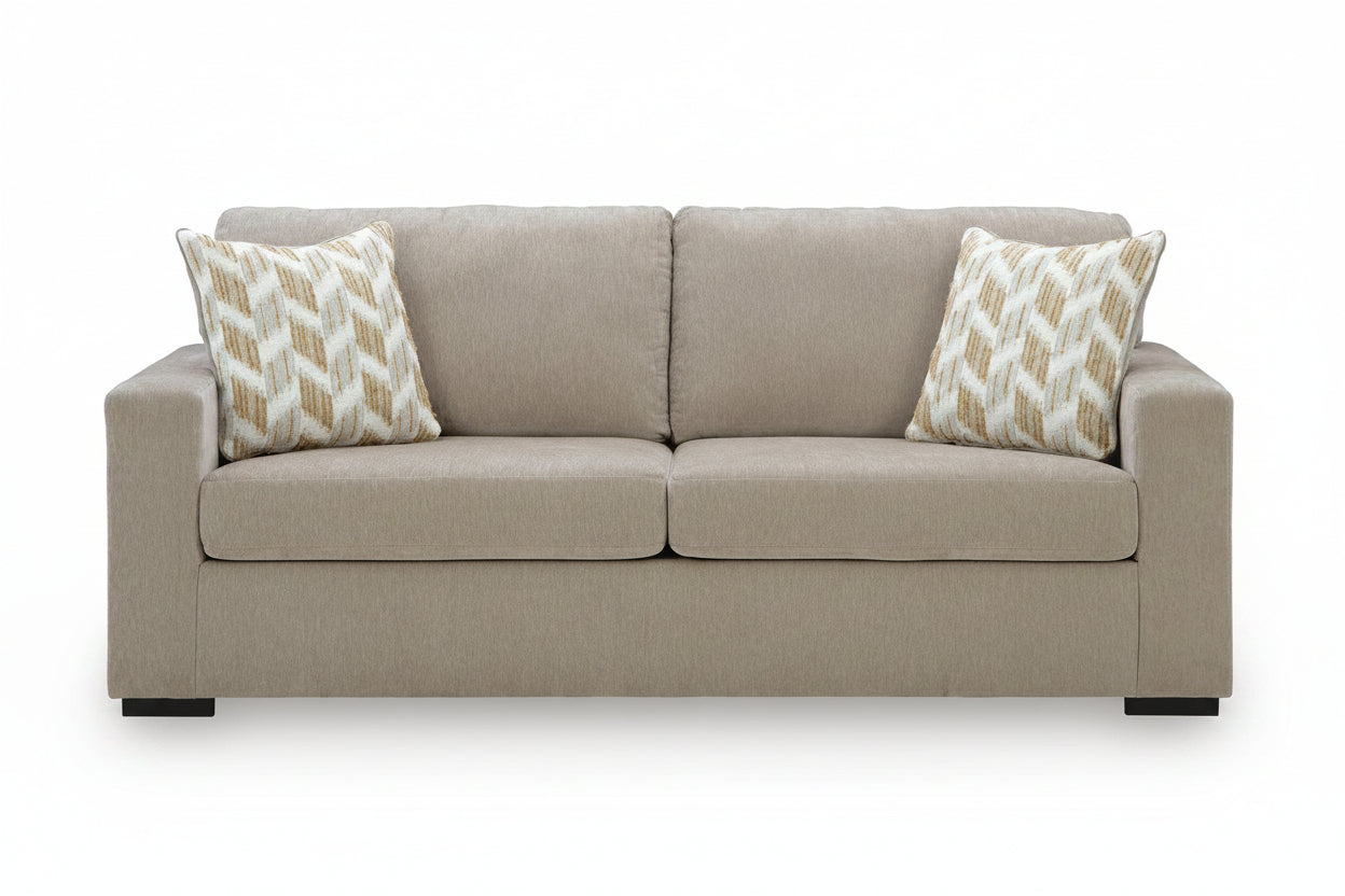 A two-seater upholstered loveseat sofa in a light taupe-beige fabric, styled with two square throw pillows featuring a cream and gold chevron pattern, set against a plain white background.