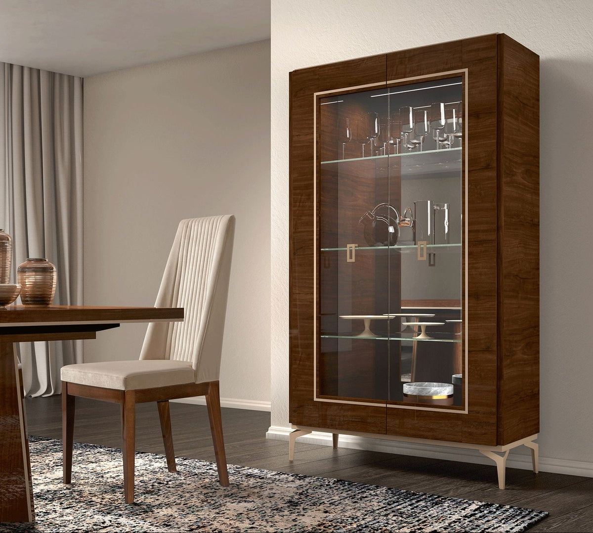 A tall dark wood display cabinet with glass doors and interior shelves stands in a modern dining room next to a dining table and chair.
