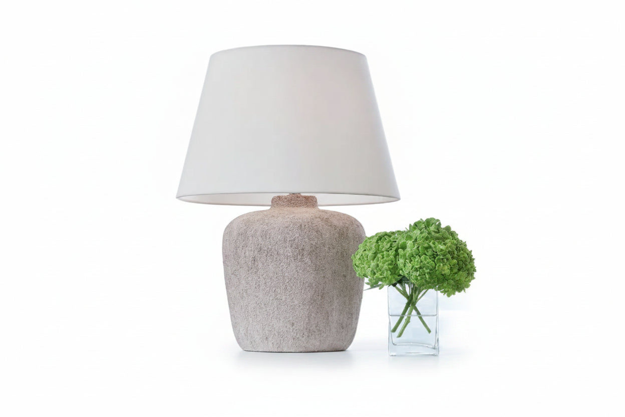 Beige textured table lamp on a windowsill with decorative plants