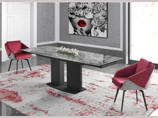 A modern grey marble dining table with a black double-pedestal base stands between two elegant red velvet chairs on a contemporary area rug.