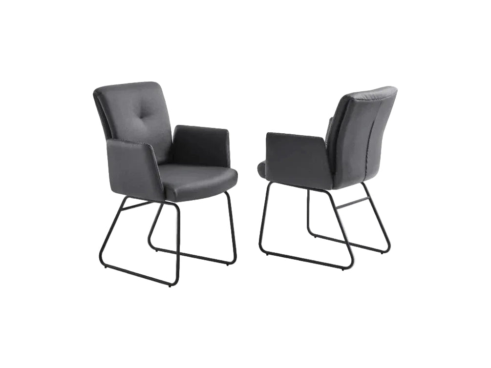 Two modern charcoal grey upholstered dining chairs with armrests and black metal sled bases stand against a white background.